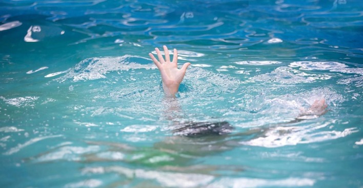 Die Hand eines Kindes schaut aus dem Wasser eines Hallenbads.
