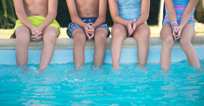 Vier Kinder sitzen am Beckenrand eines Schwimmbads.