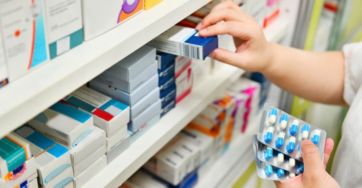 Apothekerin sortiert Medikamente im Regal einer Apotheke
