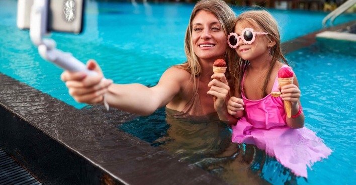 Mutter und Tochter mit Selfie-Stick am Pool