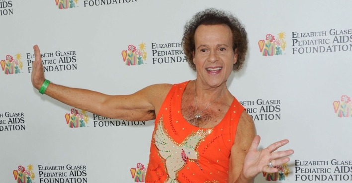 Richard Simmons, immer grinsend, wirft sich im Fitness-Outfit am Roten Teppich in Pose