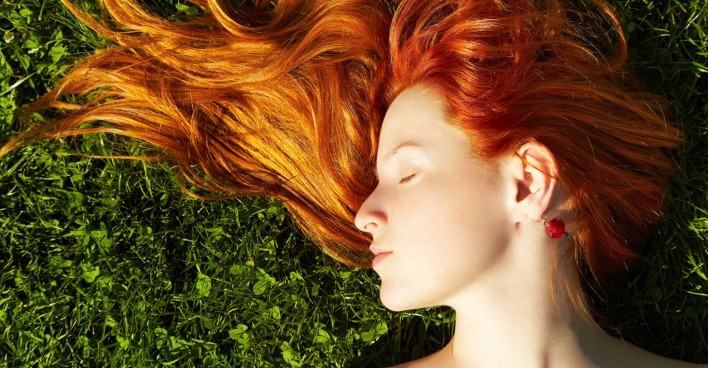 Frau mit roten Haaren liegt im Gras | Credit: iStock.com/Bakharev