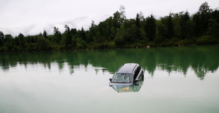 Kraftfahrzeug im Fluss Drau umgeben von Baumlandschaft