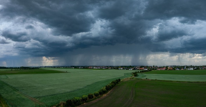 Gewitter mit Starkregen über einem grünen Feld.