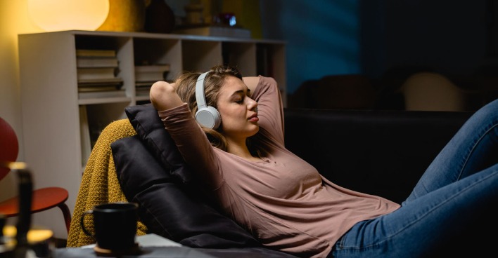 Frau liegt auf der Couch mit Kopfhörern | Credit: iStock.com/Dejan_Dundjerski