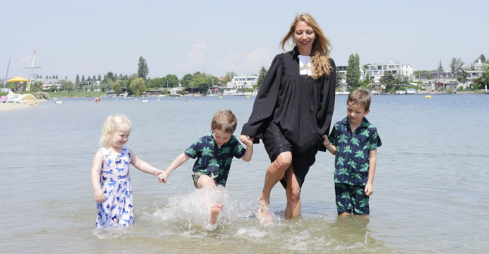 Pfarrerin steht im Talar und drei Kindern im Wasser