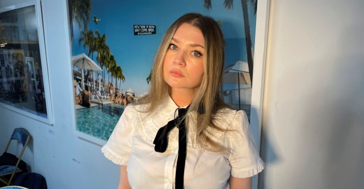 Anna Sorokin steht beim Dreh ihres Podcasts vor einem Urlaubsposter an der Wand
