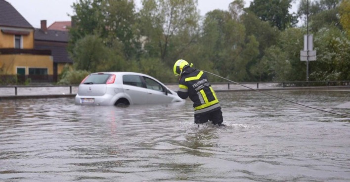 Ein Feuerwehrmann kämpft sich auf einer überflutenden Straße zu einem Auto durch.