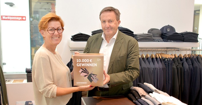 Heidi Mark überreicht Ambros Mayer (Ambros fine clothing) seine Gewinnbox. Er zählt zu den über 65 Unternehmen, die Gewinnchancen bieten.