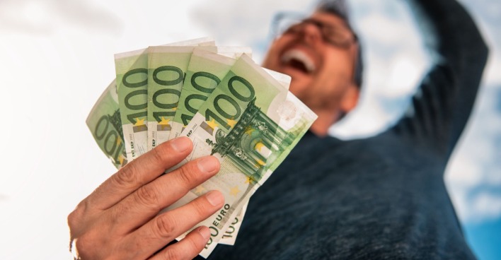 Porträt eines jubelnden Mannes mit Geldscheinen in einer Hand