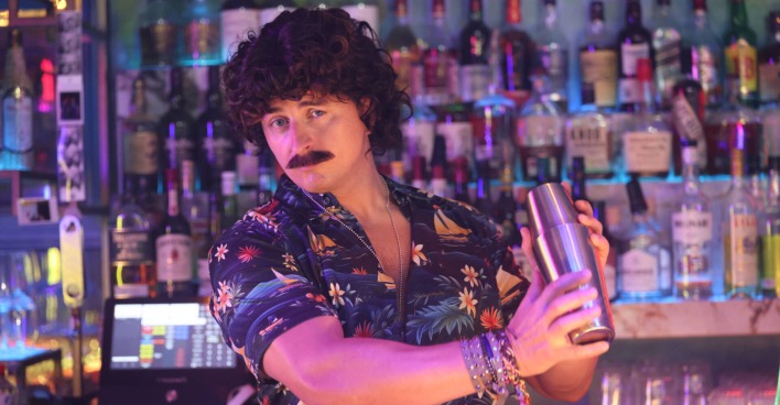 Mann mit Schnauzer steht hinter Bar und mixt Cocktails