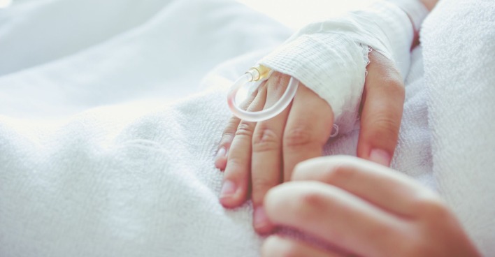 Ein kleiner Bub liegt im Spital, jemand hält seine Hand.