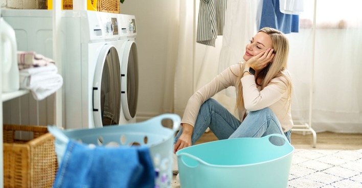 Frau sitzt vor Waschmaschine | Credit: iStock.com/FabrikaCr