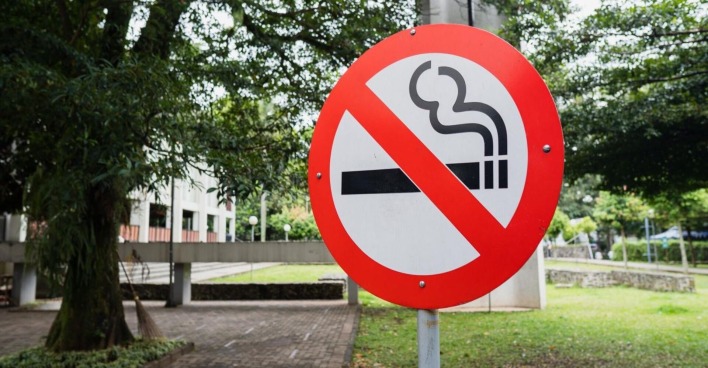 Ein "Rauchen verboten"-Schild vor eine Grünfläche.