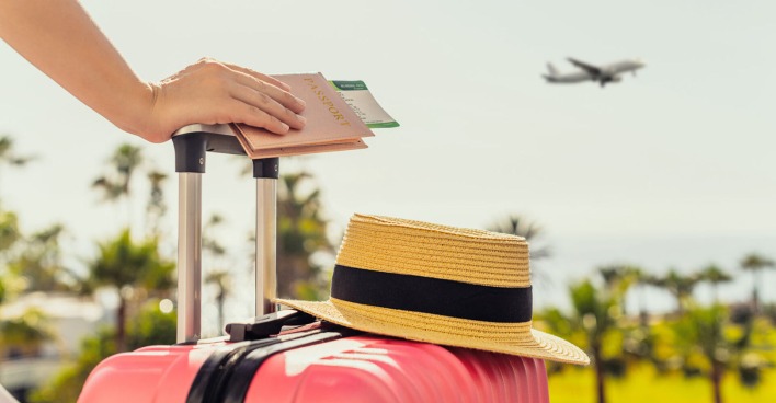 Frau hält Reisekoffer | Credit: iStock.com/FTiare