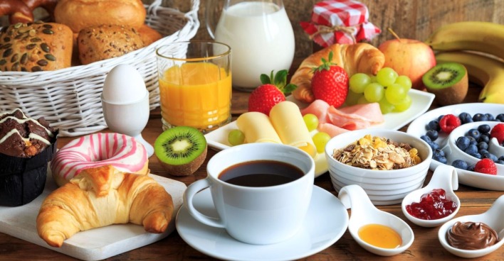Ein reich gedeckter Frühstückstisch: Zu sehen sind unter anderem eine Tasse Kaffee, Wurst, Käse, ein Korb mit Brötchen, Marmelade, Kiwis, Erdbeeren und andere Früchte.