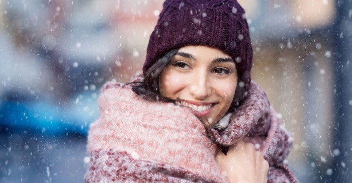 Frau steht lächelnd im Schneeschauer | Credit: iStock.com/Ridofranz