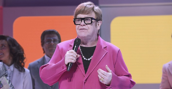Elton John in einem rosa Sakko auf der Bühne.
