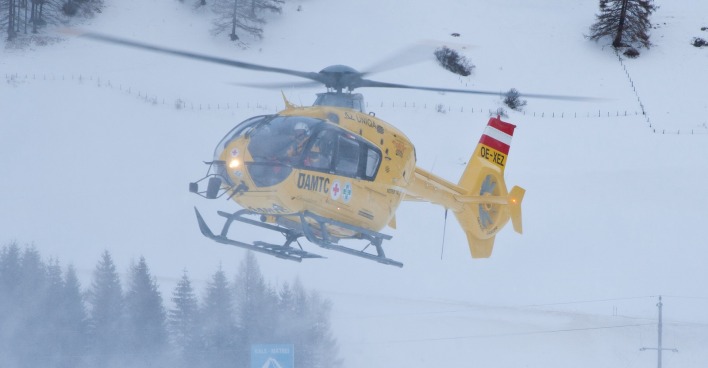 Gelber ÖAMTC-Rettungshubschrauber in einem Skigebiet.