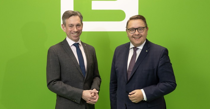 Zwei Männer in Anzügen stehen vor einer grünen Wand