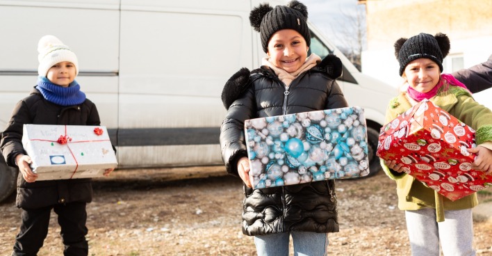 drei Kinder mit Geschenken vor einem weißen Bus