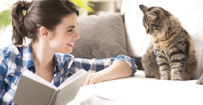 Frau sitzt mit Buch neben einer Katze | Credit: iStock.com/cyano66