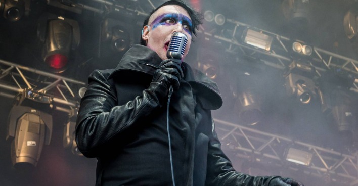 Marilyn Manson während eines Live-Auftritts, bei dem er einen langen schwarzen Mantel und blau-weißes Make-up trägt