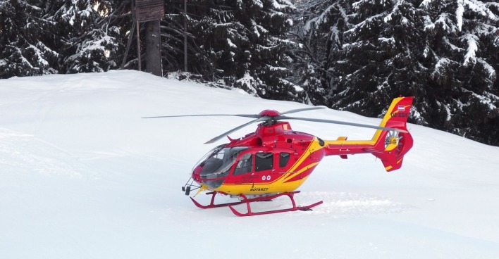Rot-gelber Rettungshubschrauber auf einer Skipiste.