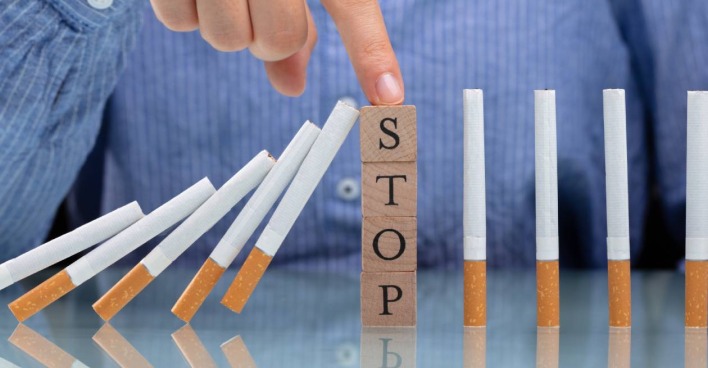 Eine Reihe umfallender Zigaretten, die von vier aufeinander gestapelten Bausteinen, auf denen das Wort "Stop" zu lesen ist, aufgehalten werden