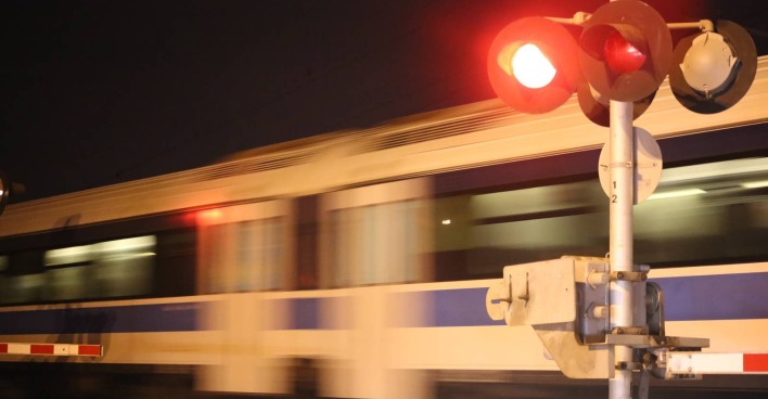 Ein verschwommen erscheinender Zug, der rasant eine Eisenbahnkreuzung überquert, während die Signalanlage rot leuchtet