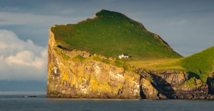 Haus auf einer Klippe einer wiesengrünen isländischen Insel