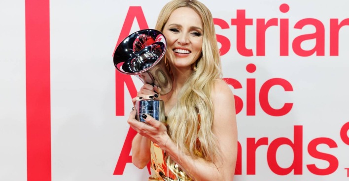 Melissa Naschenweng auf dem Roten Teppich des Amadeus Austrian Music Awards, die eine der Auszeichnungen mit zwei Händen neben ihr Gesicht hält