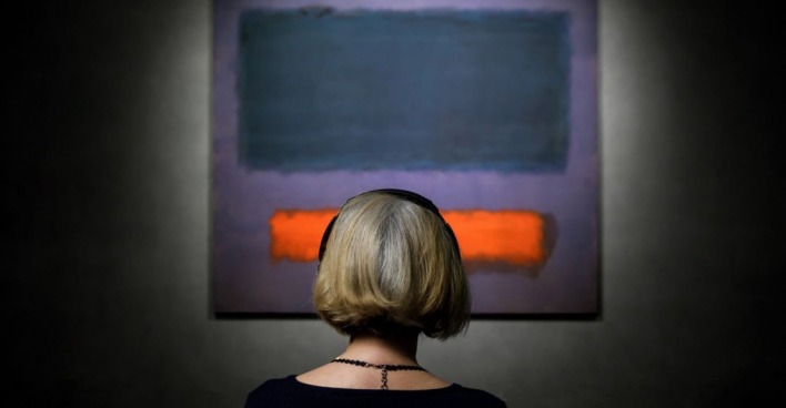Eine Frau sitzt vor dem - noch unzerkratzten - Gemälde Grey, Orange on Maroon, No. 8 von Mark Rothke. Es zeigt einen dunkelblauen und einen orangen Farblock auf ebenfalls dunkelblauem, aber etwas hellerem Untergrund.