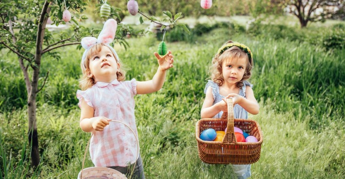 Zwei Kinder sammeln mit Körben Ostereier.