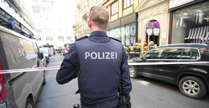 Polizist mit Schutzweste sichert Brandort in der Wiener Innenstadt ab, im Hintergrund Feuerwehrleute vor einem Gebäude in der Spiegelgasse.
