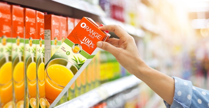 Eine Frau nimmt einen O-Saft aus dem Supermarktregal.