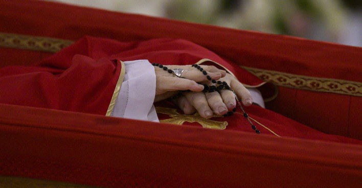 Papst Franziskus im offenen Sarg: Die gefalteten Hände halten einen schwarzen Rosenkranz, das purpurne Messgewand ist schlicht mit Goldborte verziert