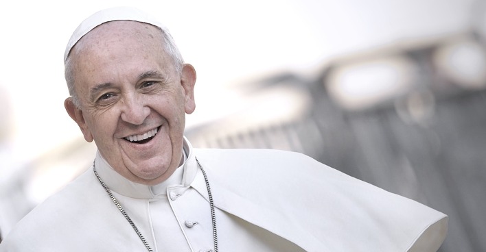 Porträt von Papst Franziskus aus dem Jahr 2013 mit freundlichem Lächeln im weißen Ornat im Freien, leicht seitlich aufgenommen.