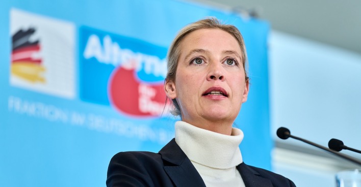 Alice Weidel, AfD-Bundesvorsitzende, spricht auf einer Pressekonferenz vor einem blauen Hintergrund mit AfD-Logo und Mikrofonen.