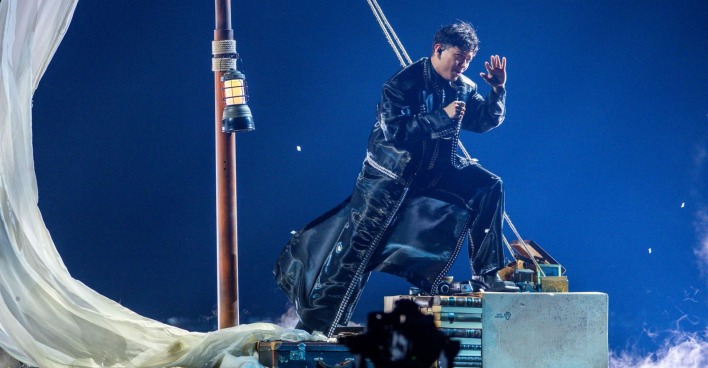 JJ beim ESC 2025-Halbfinale auf einer symbolischen Segelboot-Bühne in Schwarz-Weiß-Optik, gekleidet in langen Mantel und umgeben von Nebel.