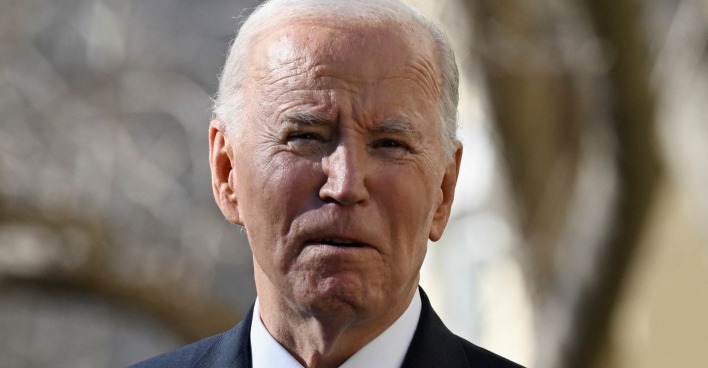 Porträt des krebskranken Joe Biden im Anzug, mit ernster Miene, vor unscharfem Hintergrund im Freien.