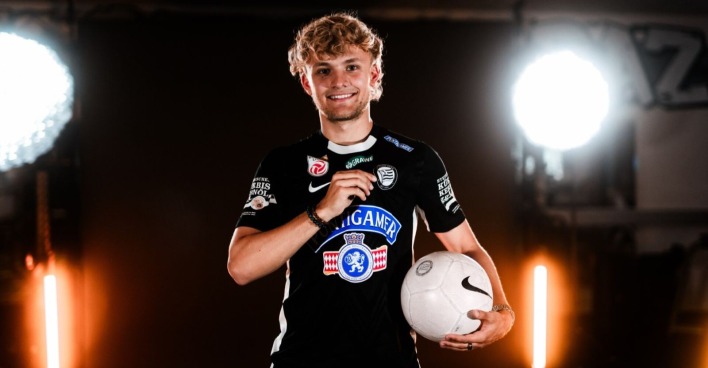 Julius Beck steht im Sturm Graz Trikot mit Ball in der Hand