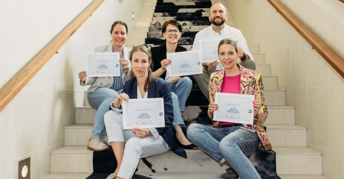 Absolventen des "Senior Marketing Professional"-Programms sitzen mit ihren Urkunden auf einer Stiege