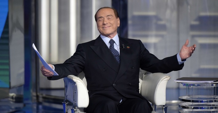Silvio Berlusconi sitzt im TV-Studio und breitet gönnerhaft die Arme aus