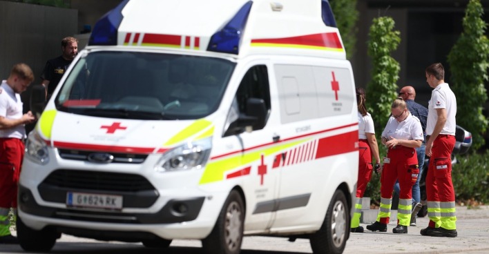 Sanitäterinnen und Sanitäter des Roten Kreuzes sowie Polizeibeamte stehen neben einem Rettungswagen im Einsatzgebiet nach dem Amoklauf in Graz.