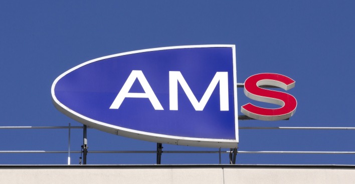 Logo des Arbeitsmarktservice (AMS) auf einem Gebäudedach vor blauem Himmel, das rote S am rechten Rand leuchtet.