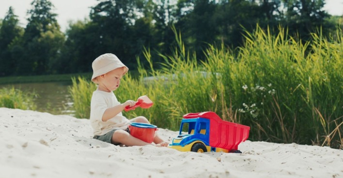 Am Strand spielt ein Junge mit Hut im Sandkasten, schaufelt Sand in einen Eimer und genießt die Natur