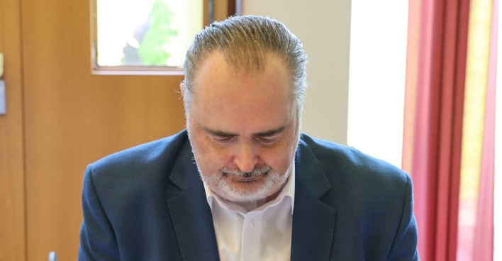 Hans Peter Doskozil blickt nach unten, trägt ein dunkles Sakko und ein weißes Hemd, im Hintergrund ein Fenster mit rotem Vorhang.
