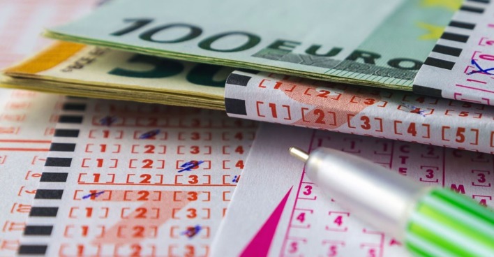 Nahaufnahme eines ausgefüllten Lottoscheins mit mehreren Euro-Geldscheinen und einem grünen Kugelschreiber.