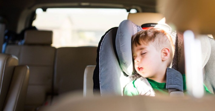 Kind schläft im Kindersitz im Auto, Sonne scheint herein, Gefahr durch Hitze und Überhitzung für Kinder im geparkten Auto.